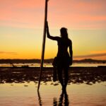 silhouette of a woman holding a surfboard on the beach during sunset